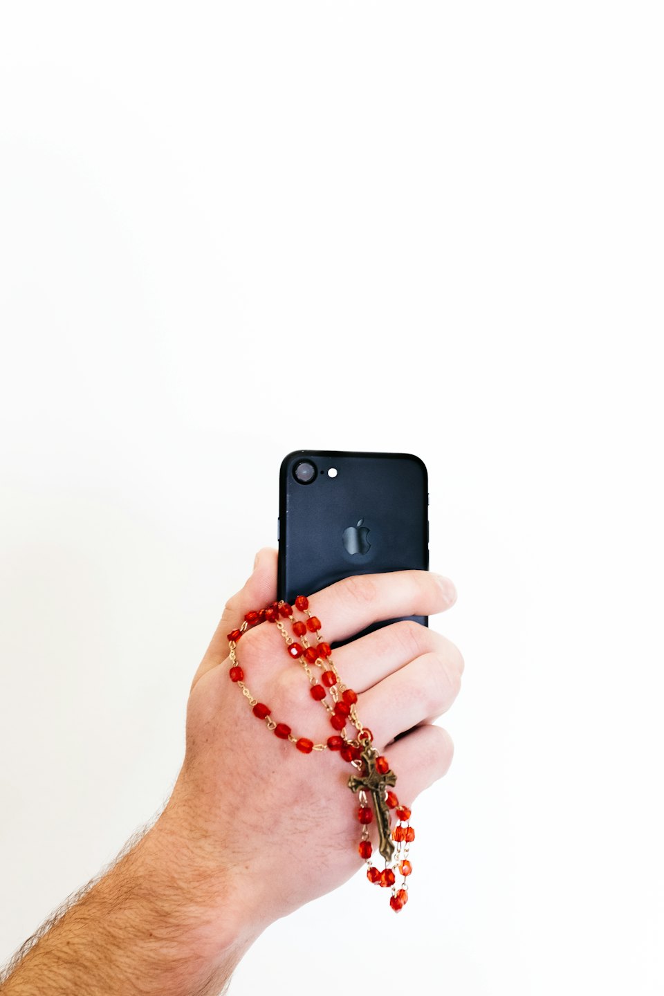 Dłoń trzyma czarny smartfon z różańcem przewieszonym przez palce.